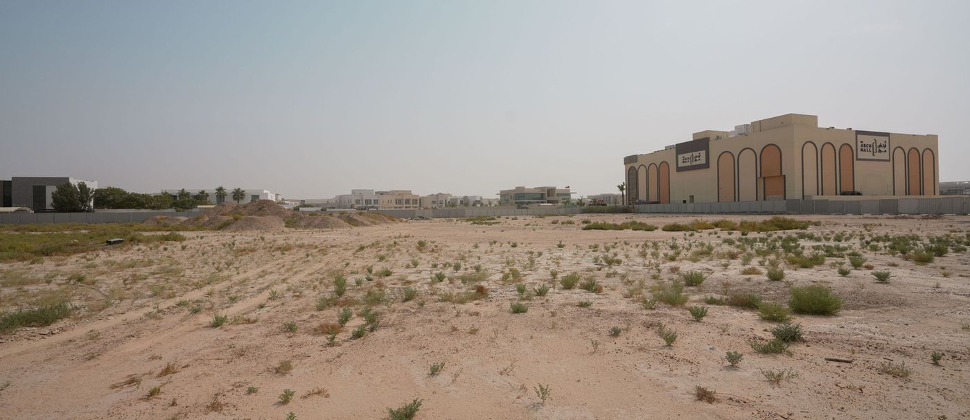 An empty sandy plot between low buildings.