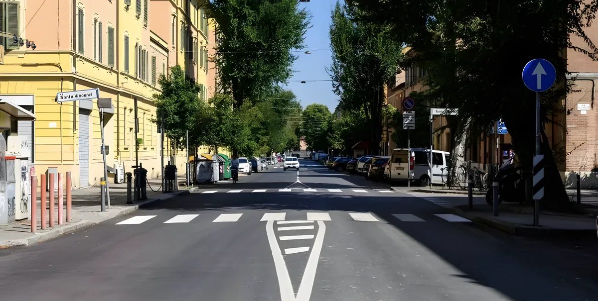A Bologna street as photographed: a wide carriageway, parked cars and a pedestrian crossing.